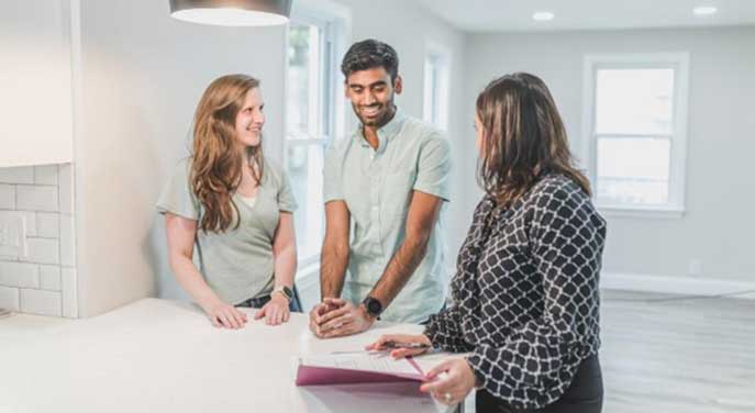 A young couple meets with a real estate agent in an empty home to look over a contract
