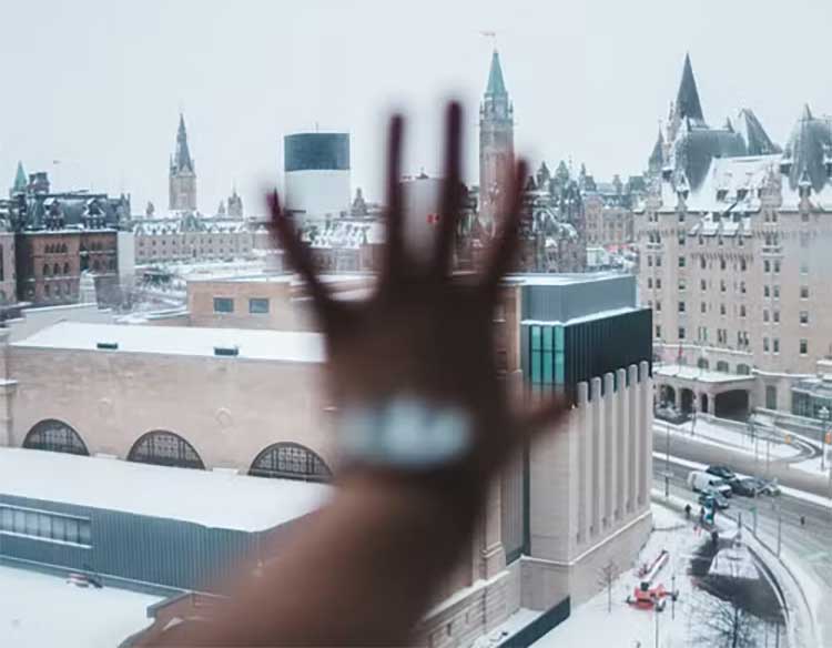 Blurred hand pressed against a window in the foreground; a snowy city skyline with tall spires and buildings in the background.