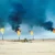 Gas flares burning at an oil field in a sandy desert, with thick black smoke rising from multiple towers.