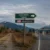 Border checkpoint on a highway with a green sign reading 'Innovation Future' and a US label; a Canada sign sits along a dirt path to the left with mountains in the distance.