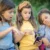 Three girls sitting outdoors on grass, looking at a smartphone together.